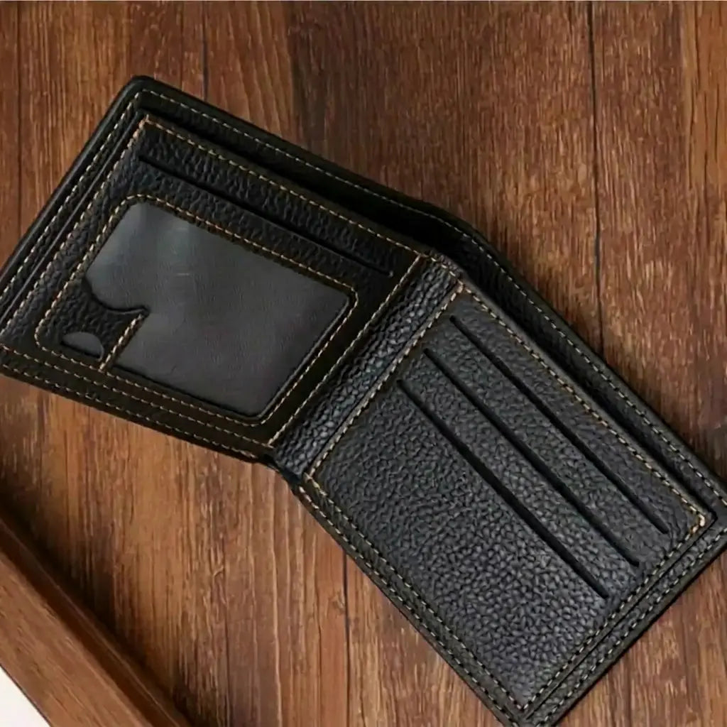  Interior of the black leather Arlen wallet opened flat on a wooden surface, showing multiple card slots and a clear ID window with tan contrast stitching.